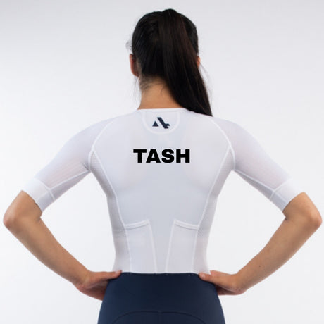 Person wearing a white trisuit with 'TASH' personalised name print on a light gray background