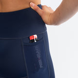 Navy blue athletic triathlon shorts with a pocket containing a drink satchet on a light gray background