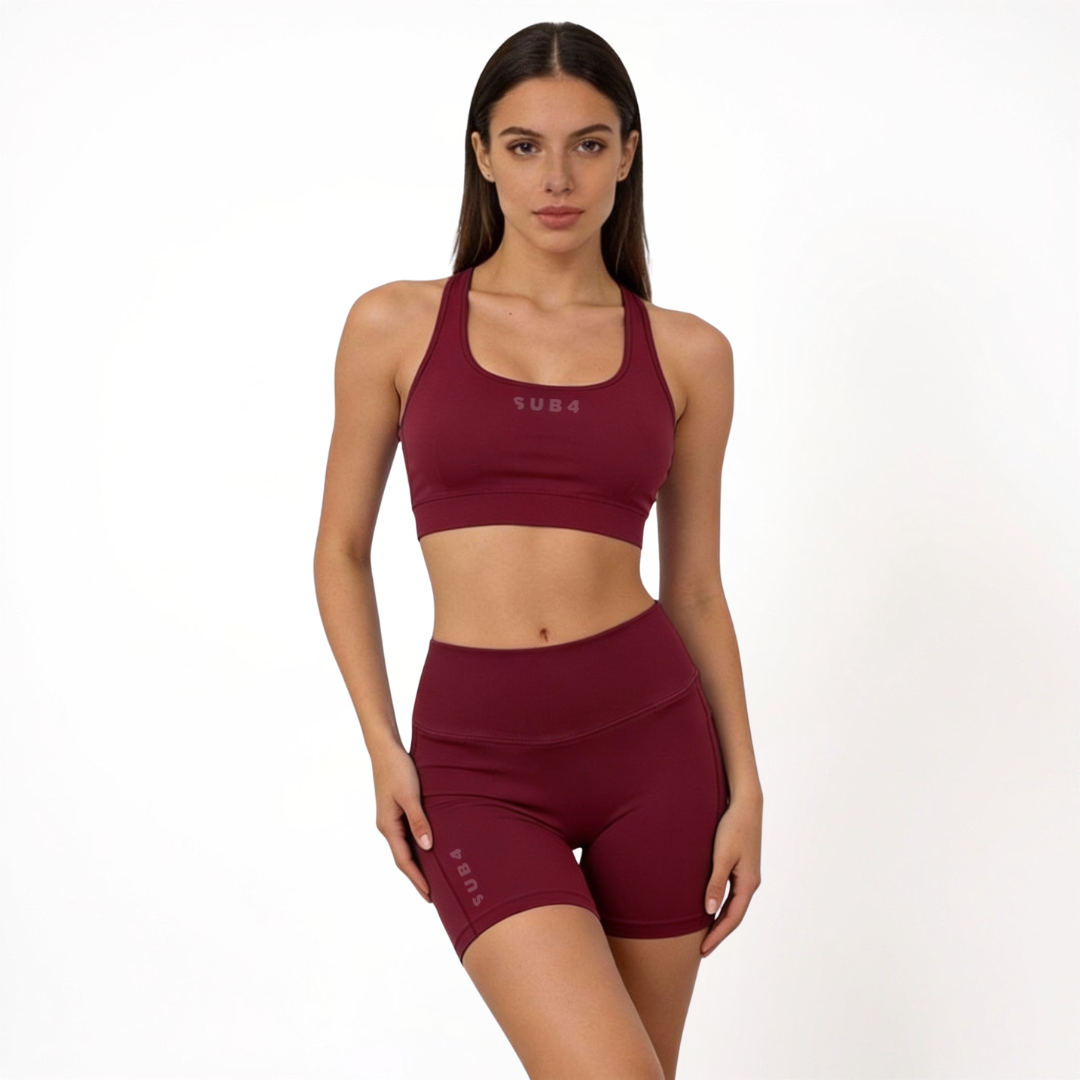 Woman wearing a maroon red sports bra and athletic shorts set on a white background